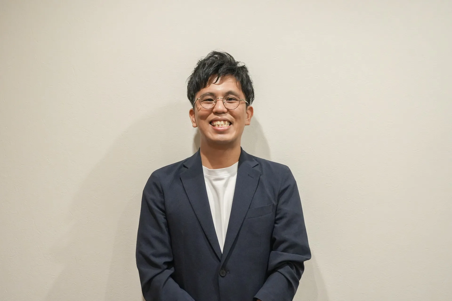 眼鏡をかけたネイビージャケット姿の男性が笑顔で立っている